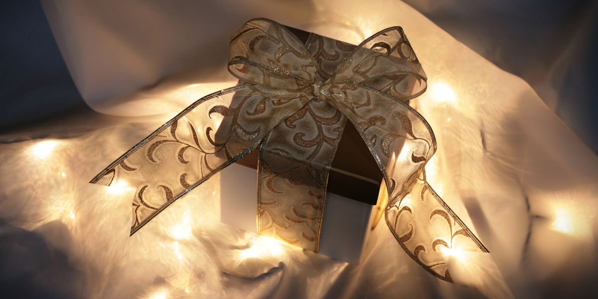 Gift box wrapped with a decorative gold ribbon, illuminated by soft glowing lights in the background